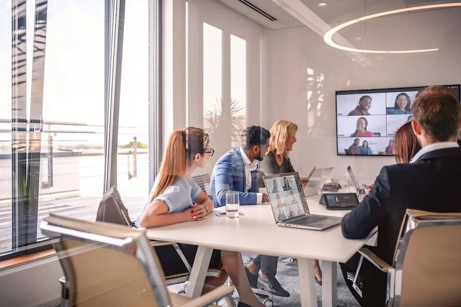 people sitting at a conference table, looking at virtual meeting attendees on a wall display.
