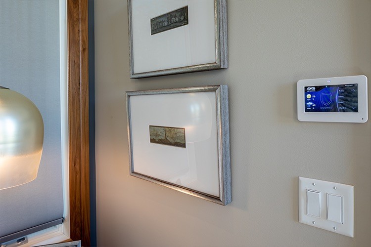  home security keypad on a wall above a double-gang light switch