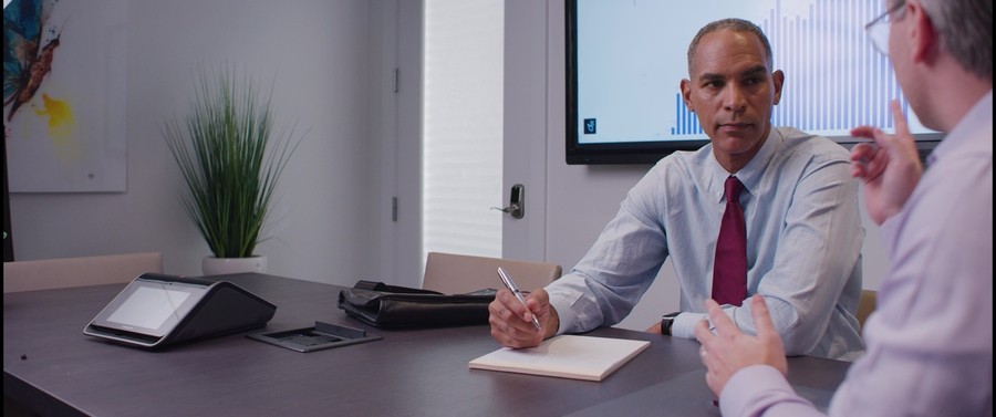 two people sit at a conference room table with a Crestron tabletop system on top.