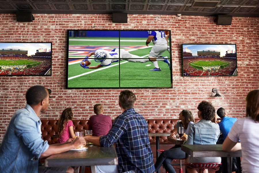 A crowd of people watches a football game on a big screen TV at a sports bar