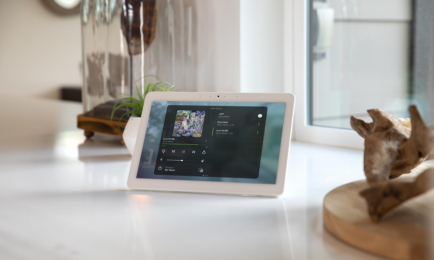 Smart home control tablet on a white countertop displaying music playlist
