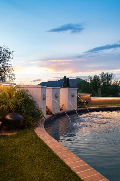 Curved pool at sunset featuring stone water fountains and integrated LED perimeter lighting