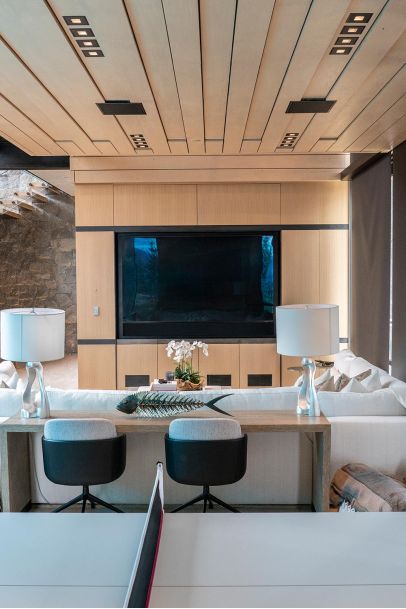 Living area with a wood-slat ceiling, integrated TV, and a long desk with white table lamps