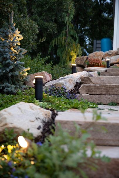 Outdoor stone staircase illuminated by black bollard landscape lighting at dusk