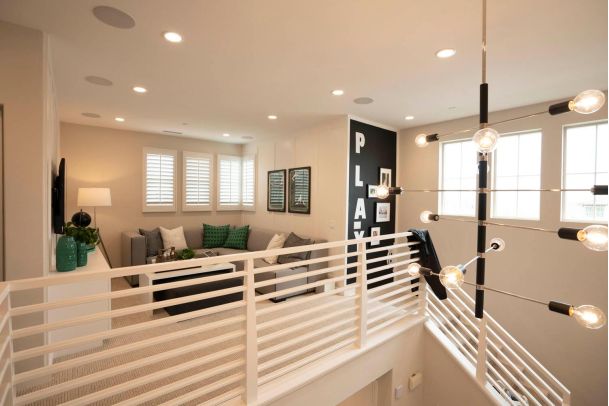 Modern loft living area with a gray sectional sofa, white railings, and a Sputnik chandelier