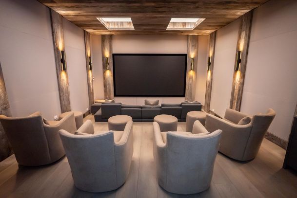 Home theater with tiered beige armchairs, wood-beamed walls, and warm vertical sconces