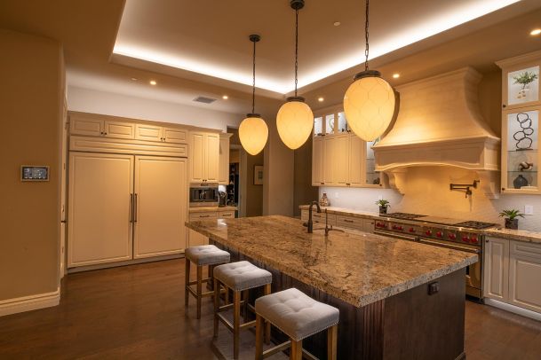 Kitchen island with granite countertop, tufted bar stools, and three large oval pendant lights