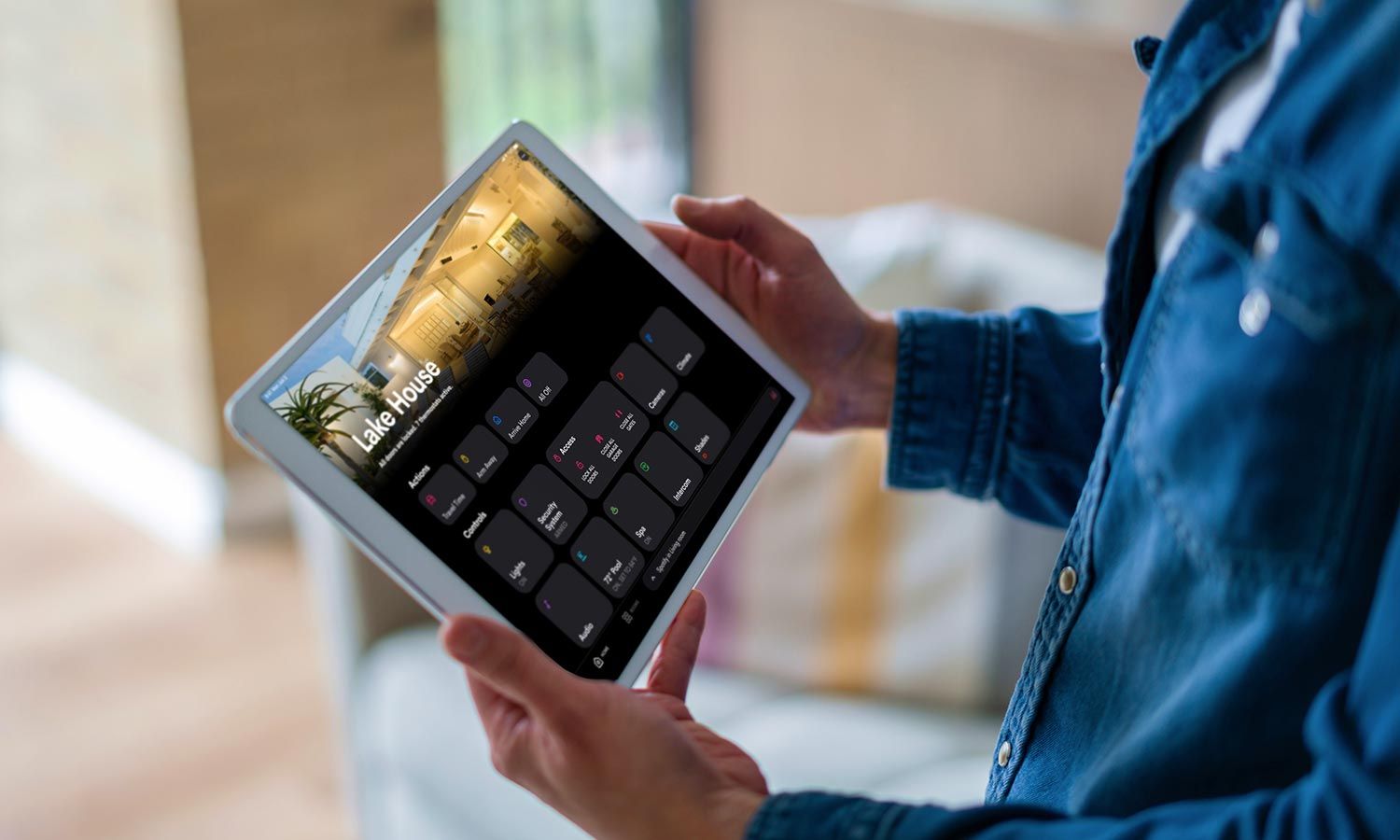 Person holding a tablet displaying smart home controls labeled Lake House