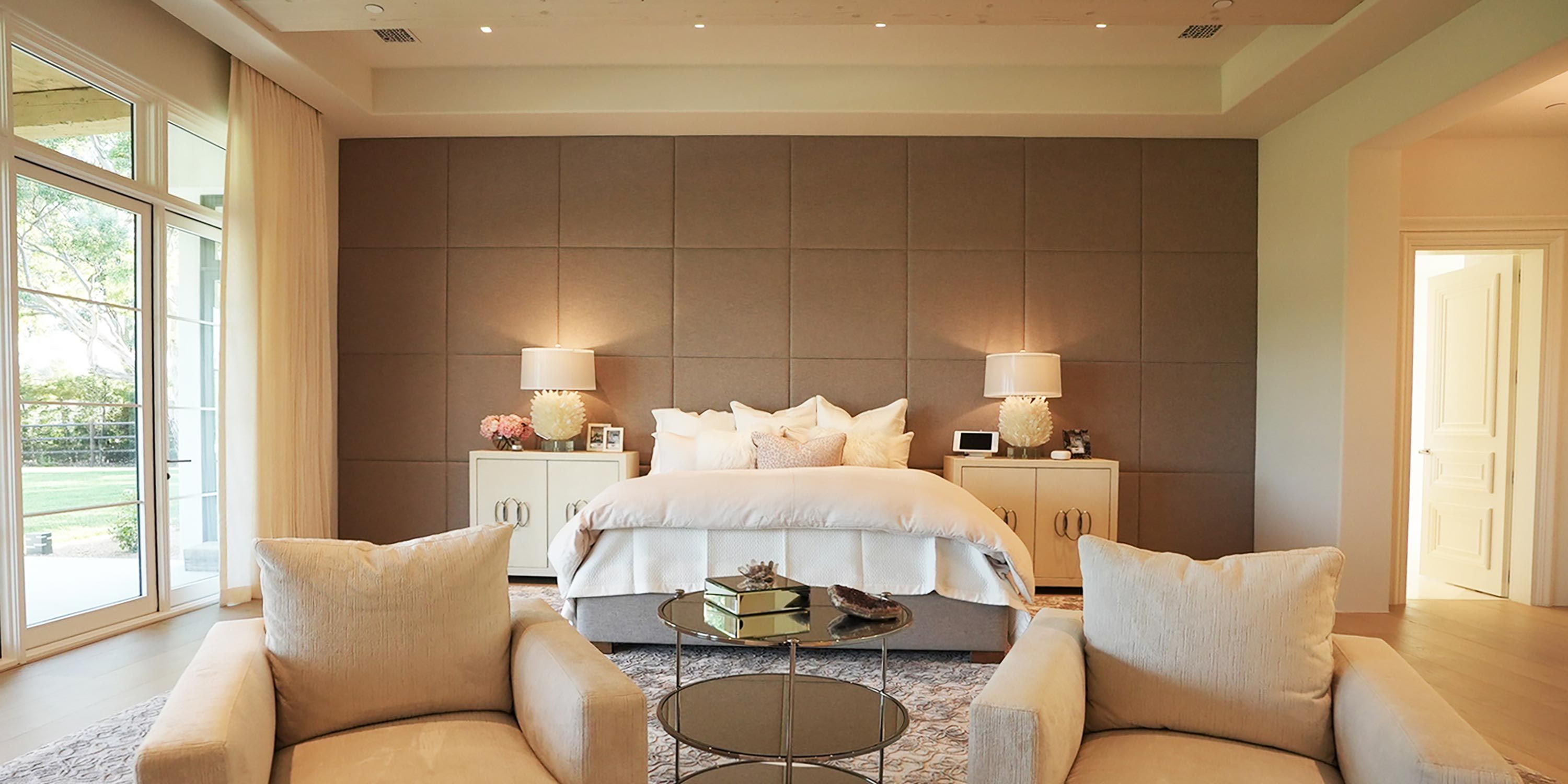 A serene bedroom with neutral tones, soft lighting, and a plush bed centered between bedside tables.