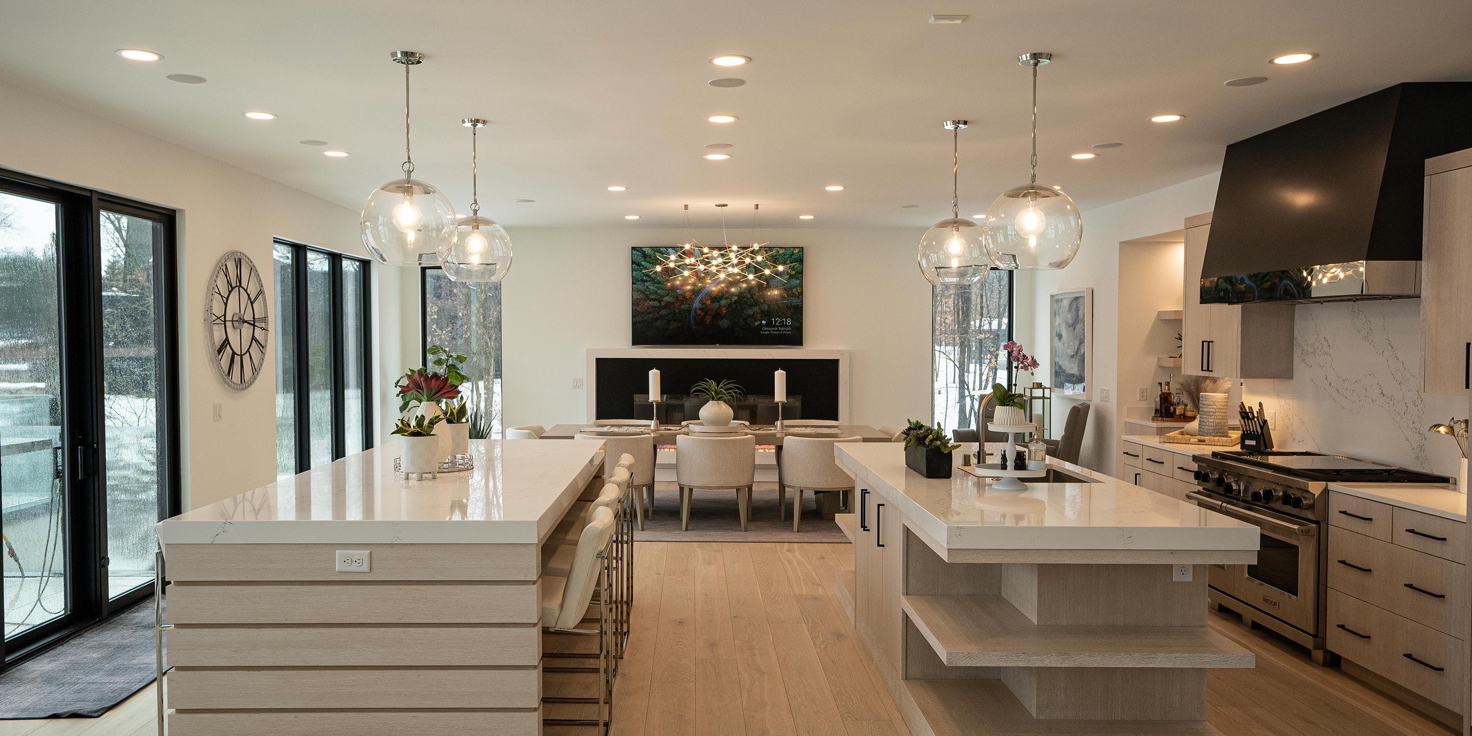 An open-concept kitchen with a large island and a dining table, featuring a television in the background and soft lighting.