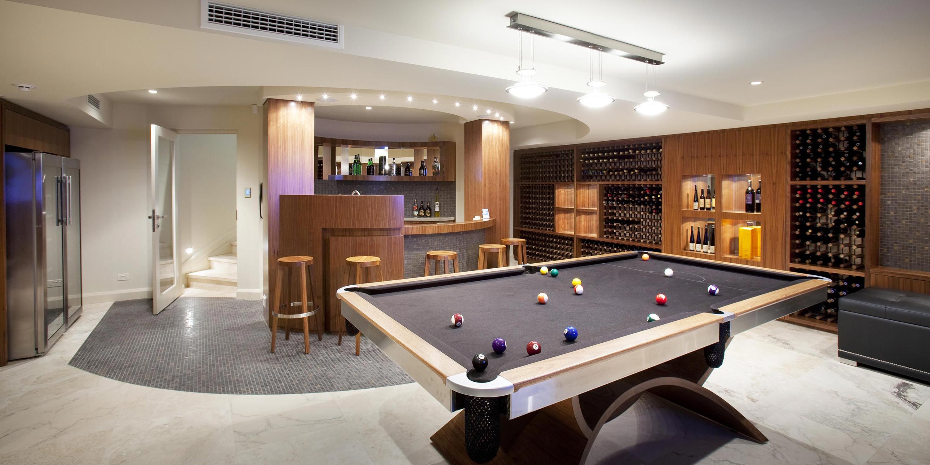 A luxurious game room featuring a pool table, a stylish bar area with stools, and extensive wine storage racks along the walls.