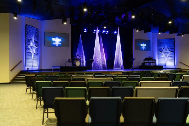 Another view of the church auditorium showing the stage with conical decorations, a drum set, and music stands. Two large screens display a "Welcome" message.