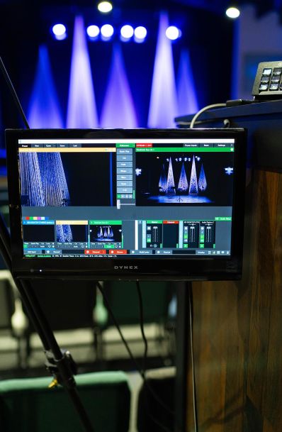 A computer monitor displaying a live video feed of the stage in the church auditorium, showing the conical decorations and stage lighting.